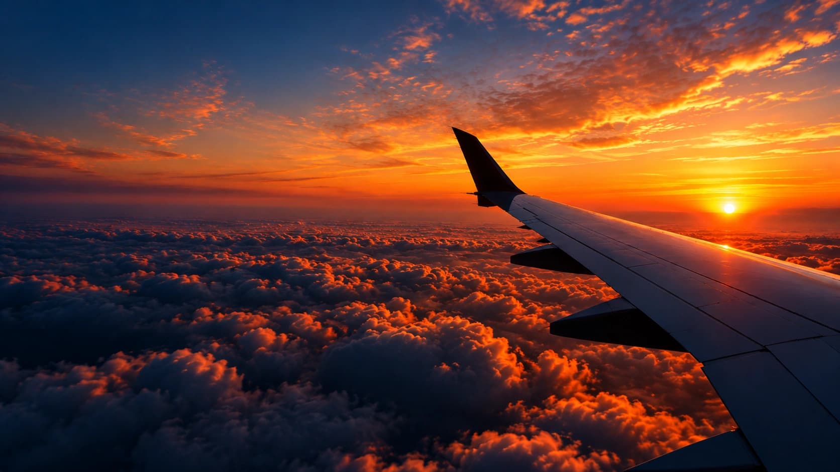 Avião sobrevoando um mar de nuvens ao pôr do sol, com o céu em tons de laranja e amarelo.